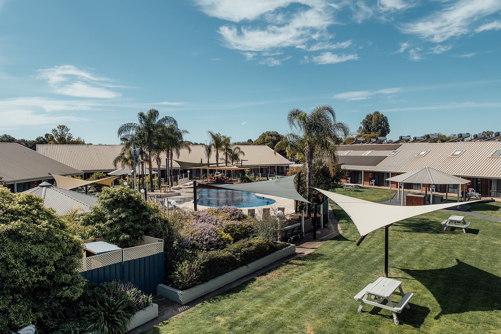 Resort courtyard seen from above, with the pool, shade sails and lawn