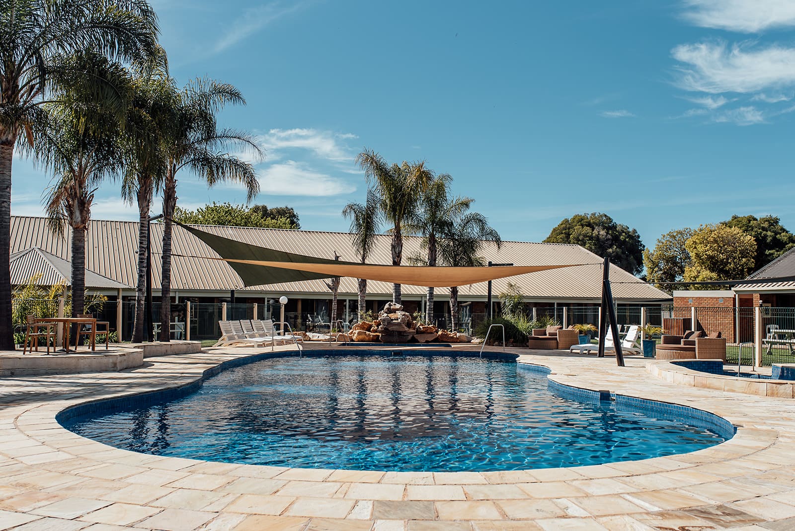 Outdoor pool surrounded by paving and palm trees, with the motel wings behind