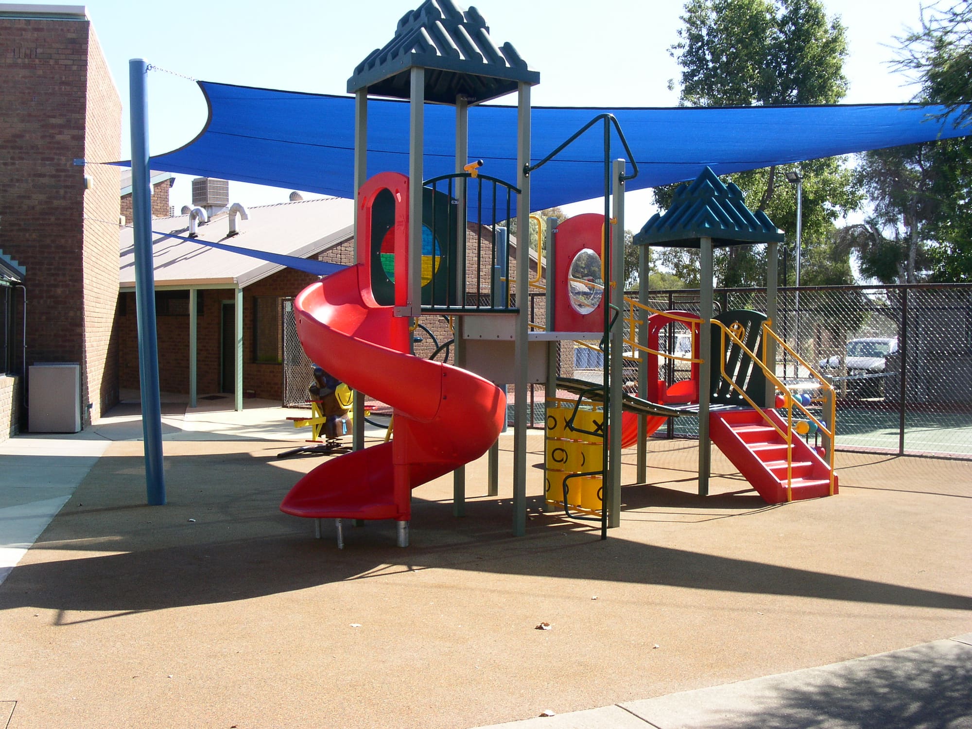 Children's playground with a red spiral slide under a blue shade sail