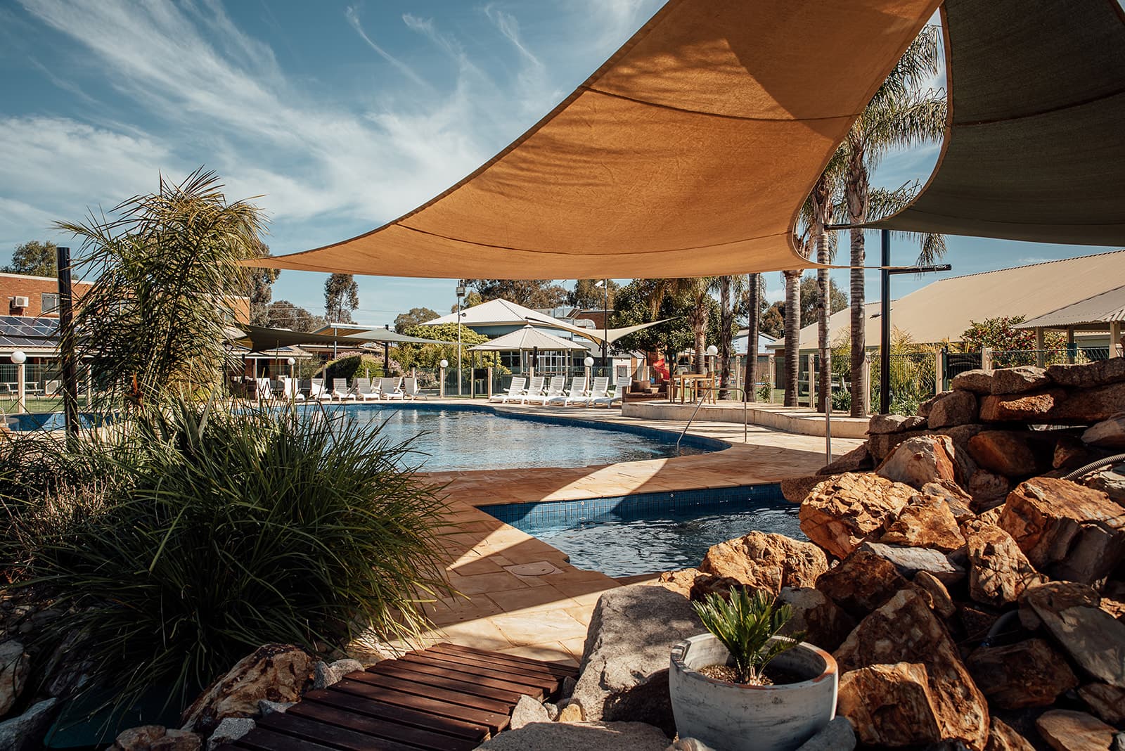 Pool beneath an orange shade sail, with a rock garden in the foreground